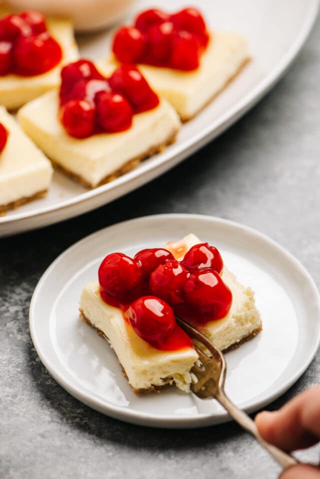 a fork cutting into a cheesecake bar topped with cherries