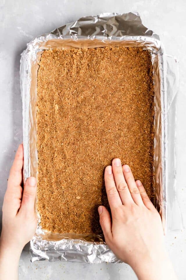 Pressing a graham cracker crust into a pan.