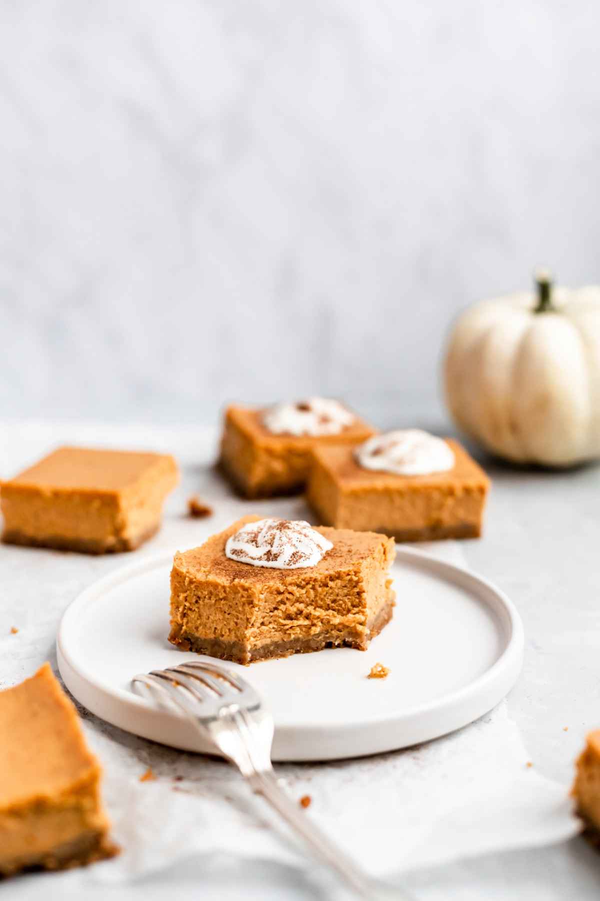 Pumpkin cheesecake bar on a white plate with a bite missing.