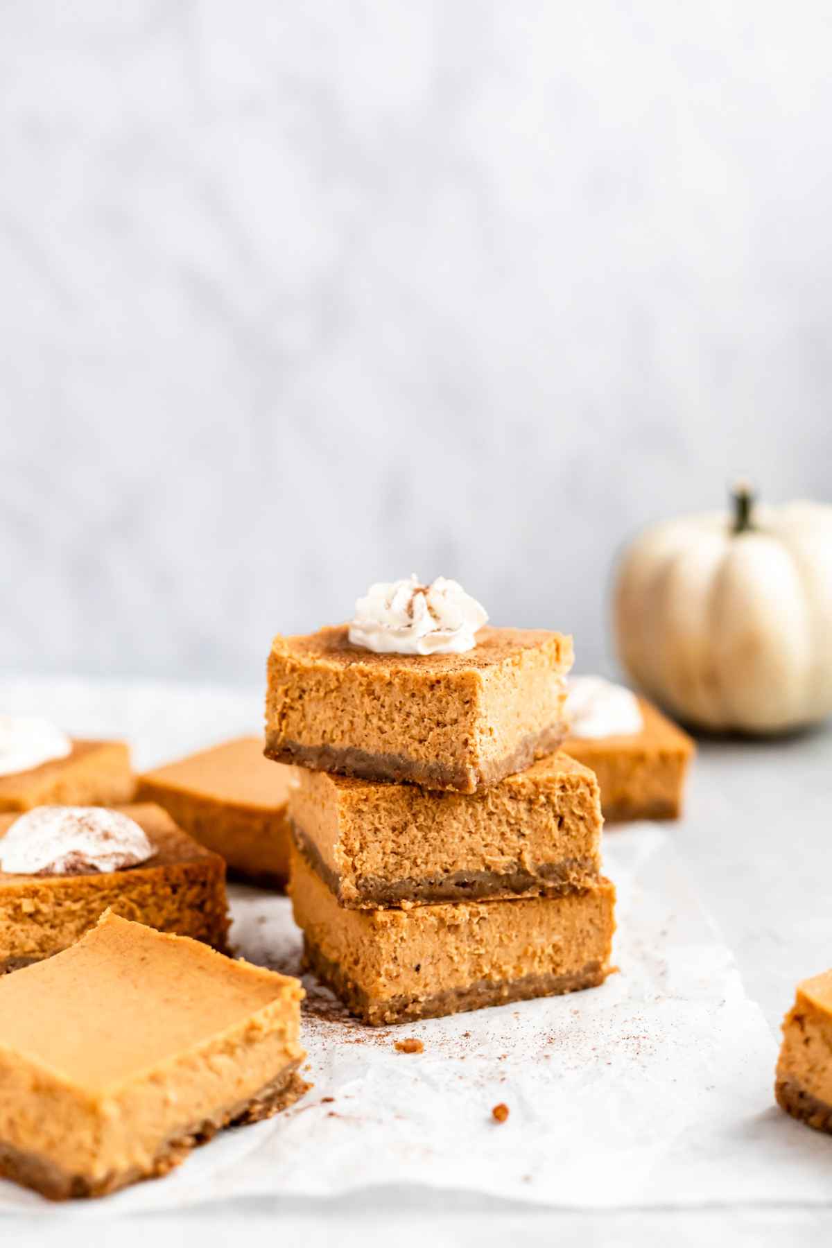 Pumpkin cheesecake bars stacked and topped with whipped cream.