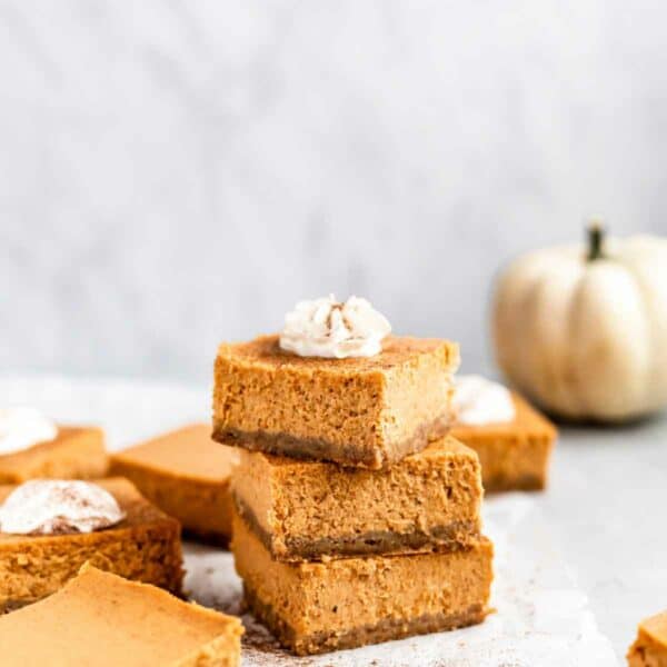 Pumpkin cheesecake bars stacked and topped with whipped cream.