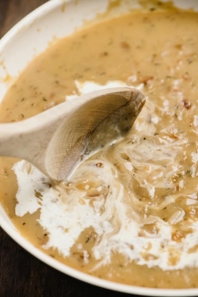 stirring cream into gravy with a wooden spoon
