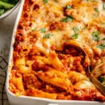 Spooning out a serving of baked ziti from a white casserole dish.