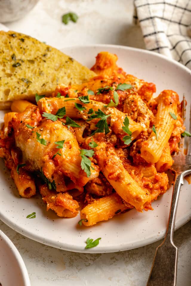 Baked ziti garnished with parsley and served with garlic bread.