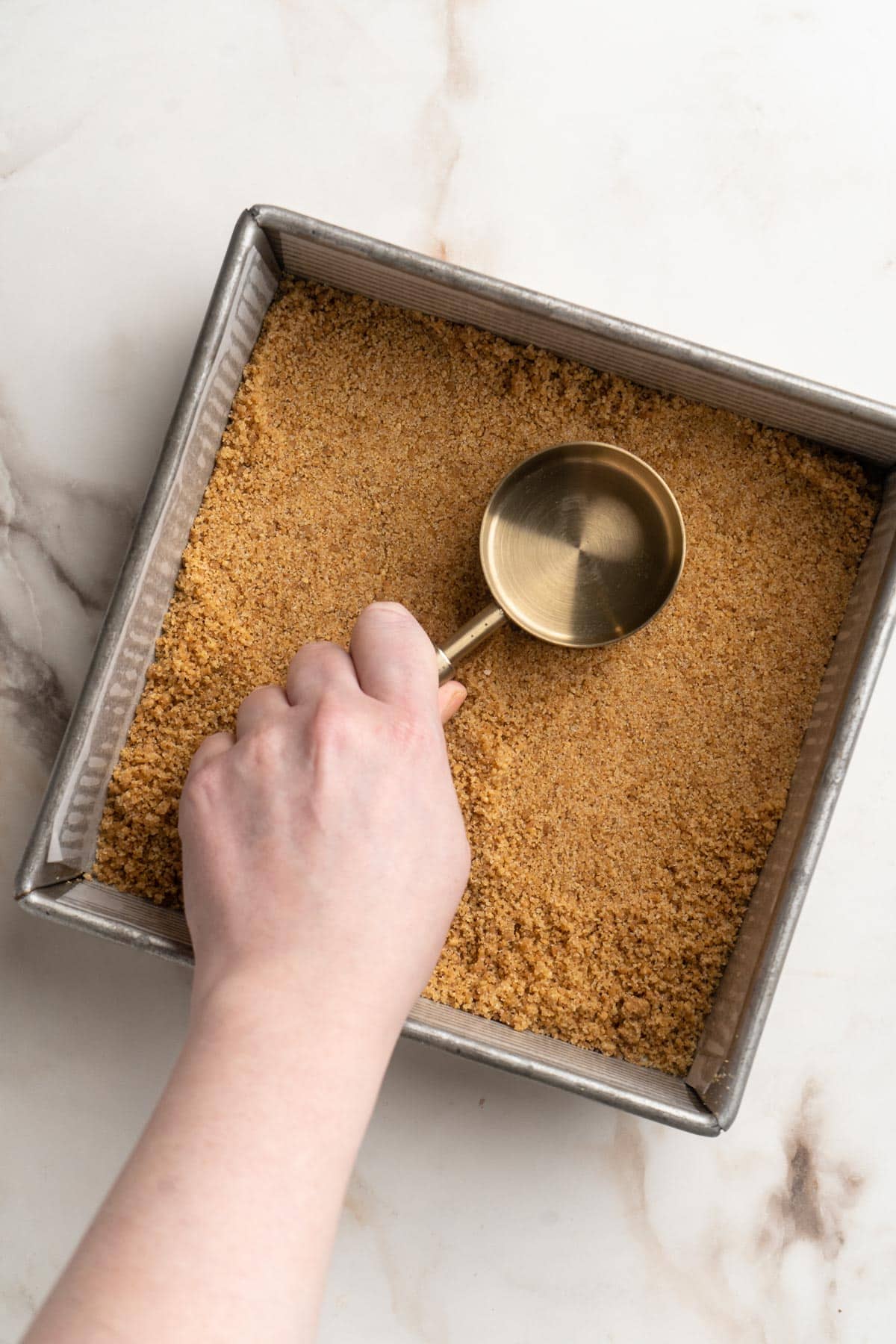 Pressing graham cracker crust into a square pan.
