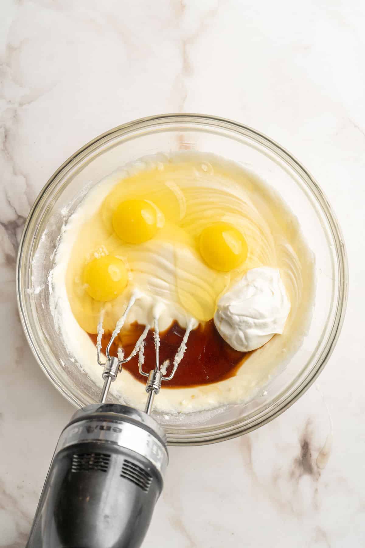 Mixing eggs, vanilla and sour cream in with cream cheese mixture.