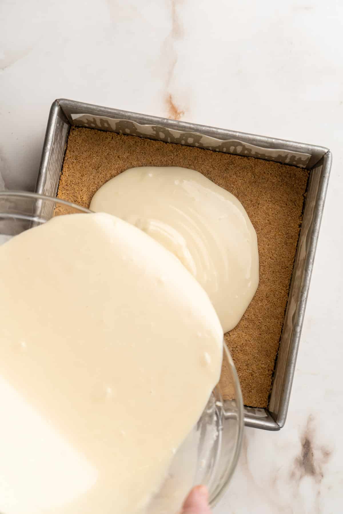 Pouring cheesecake filling over graham cracker crust.