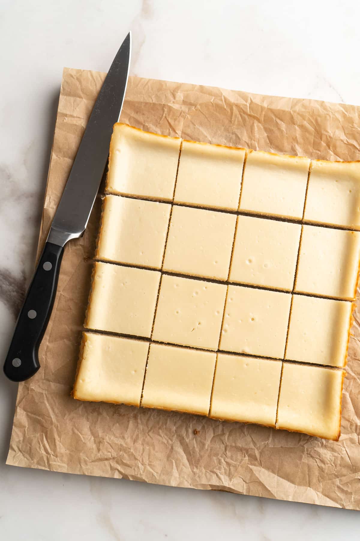 Cutting cheesecake into bars on parchment paper.