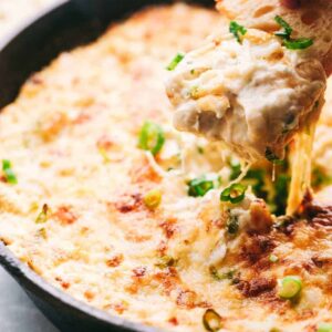 Dipping a cracker into hot crab dip from a skillet.