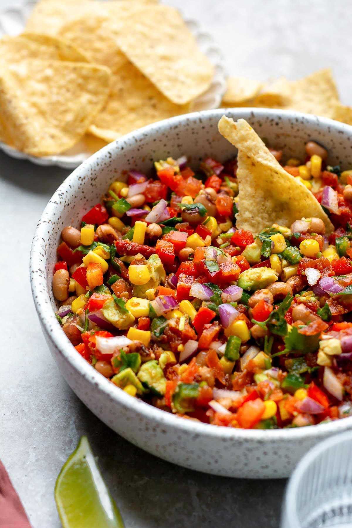 Cowboy caviar in white bowl with tortilla chips.