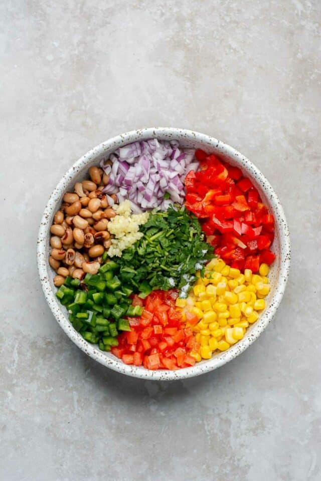 Corn, black-eyed peas, red onion, tomatoes and cilantro added to a white bowl.