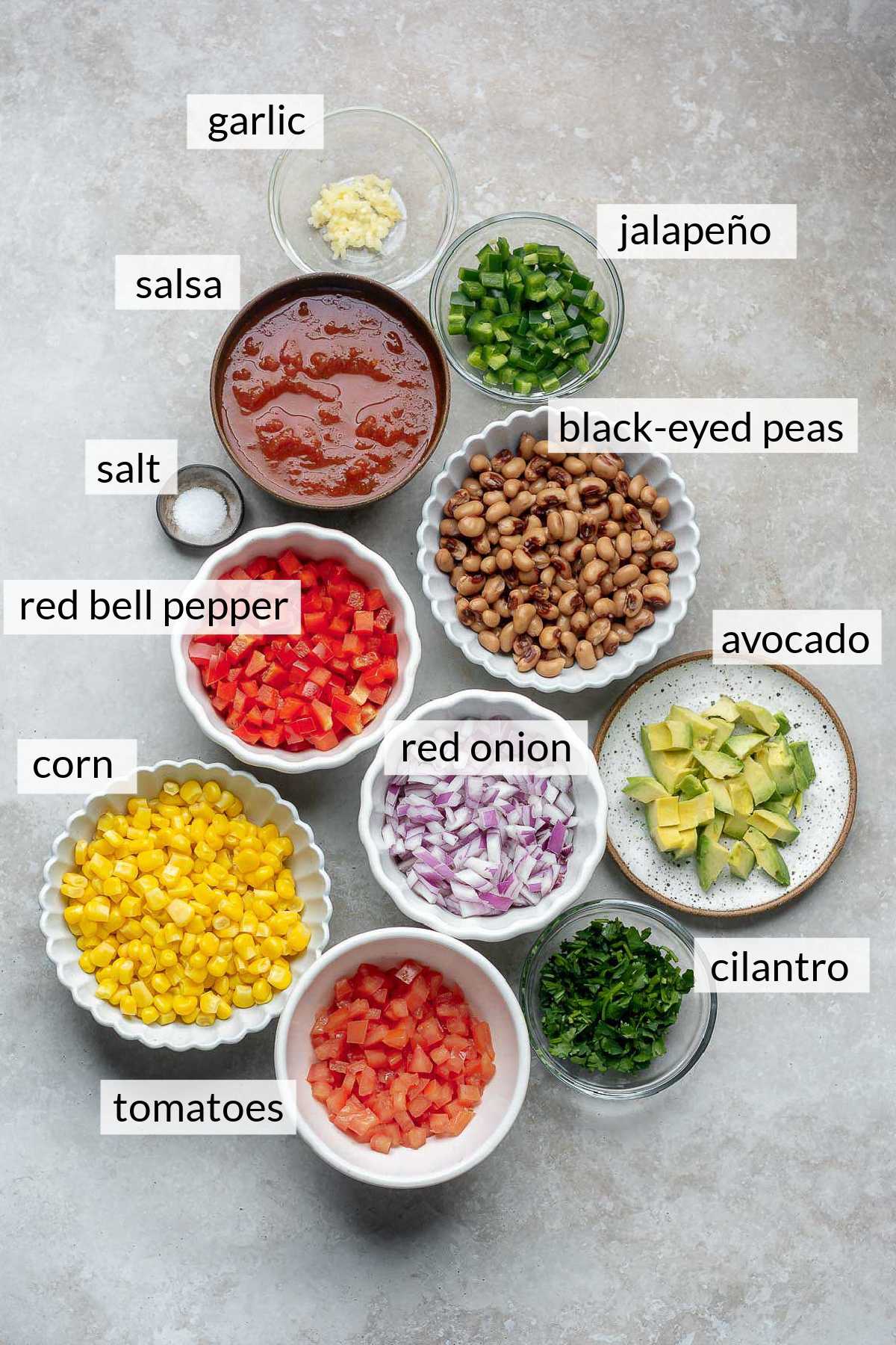 Black-eyed peas, salsa, avocado, corn, red onion and tomatoes divided into small bowls.