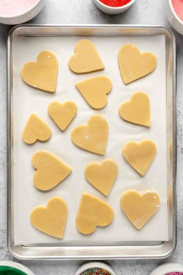 Heart-shaped cut out cookie dough on a parchment lined baking sheet.