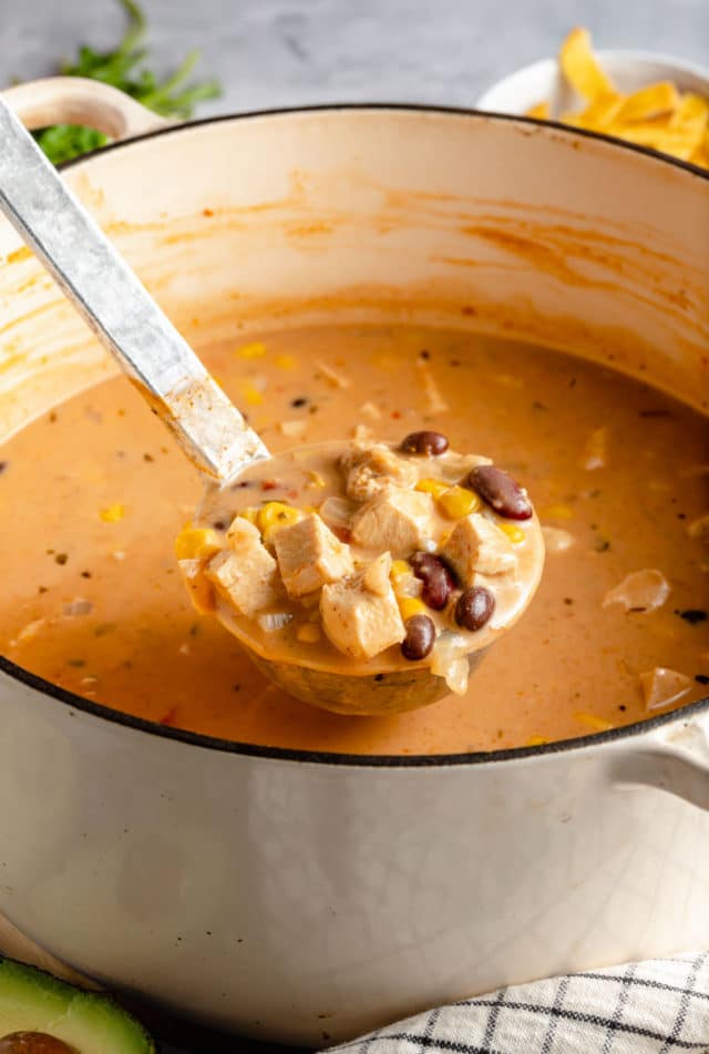 spooning creamy chicken tortilla soup out of a large pot 
