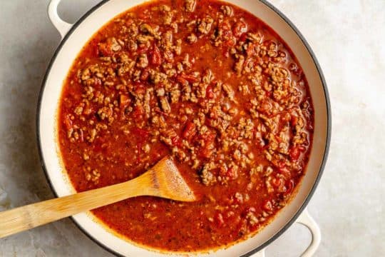 stirring meat sauce in a large pot with a wooden spoon