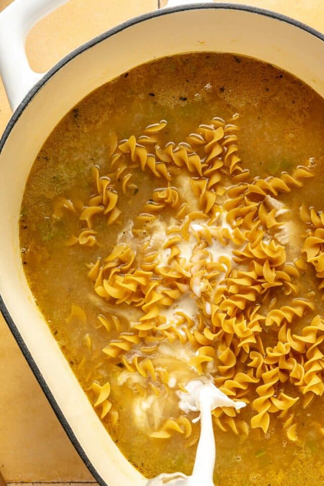 Pouring cream into soup with noodles.