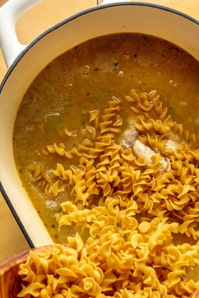 Adding noodles into broth cooking in a pot.