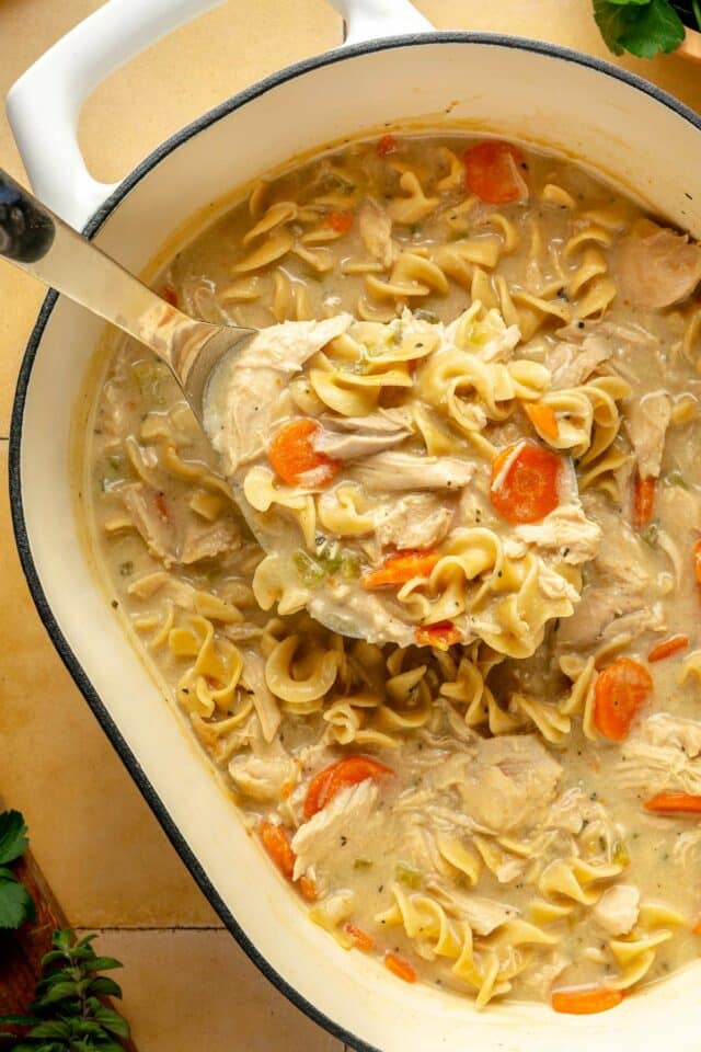 Using a ladle to serve creamy chicken noodle soup out of a pot.