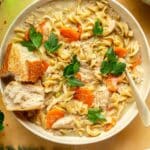 Bowl of creamy chicken noodle soup with crusty bread on top.