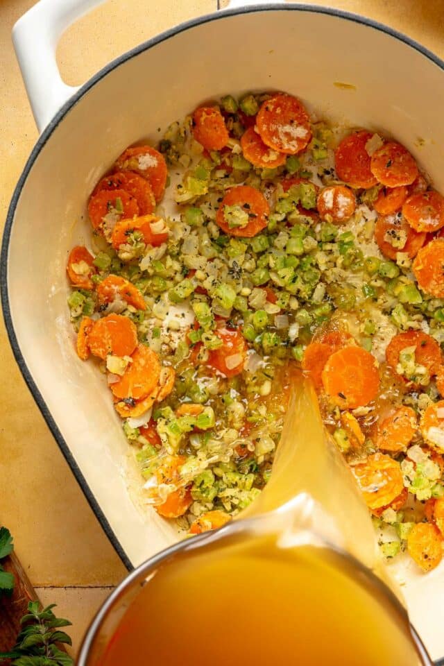 Pouring broth into a pot with vegetables.