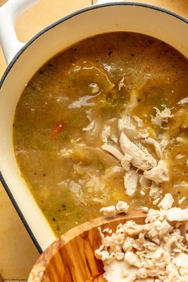 Adding shredded chicken into soup.