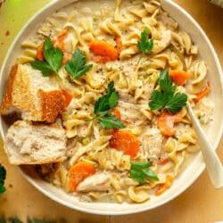 Bowl of creamy chicken noodle soup with crusty bread on top.