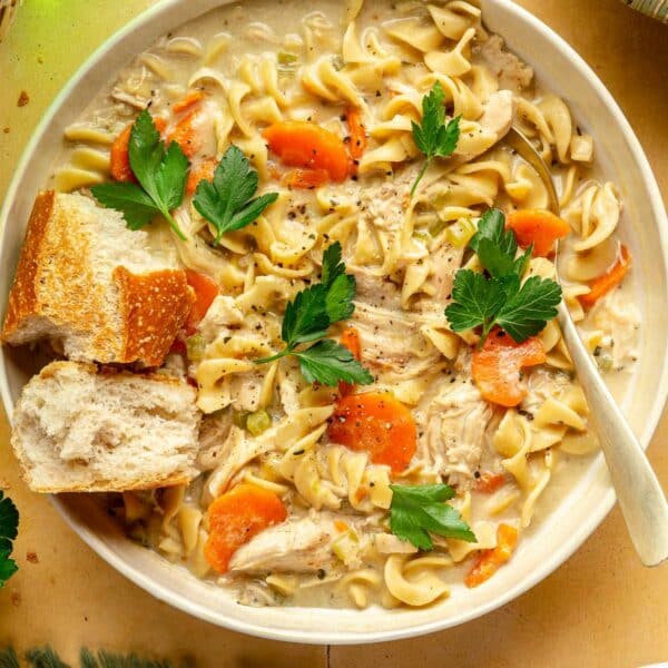Bowl of creamy chicken noodle soup with crusty bread on top.