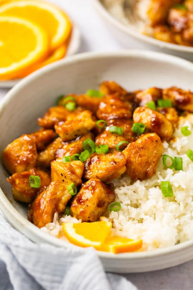 Orange chicken garnished with green onions and a slice of orange.