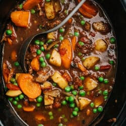 cooked vegetable beef soup in a slow cooker with a ladle