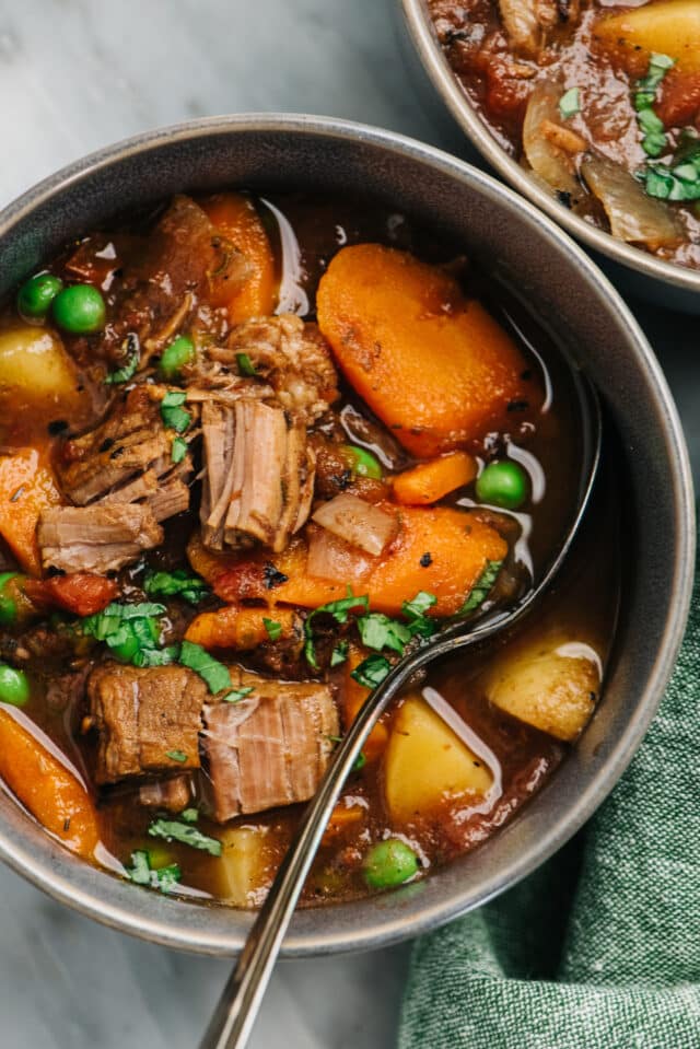 bowl filled with vegetable beef soup that includes carrots, potatoes and peas