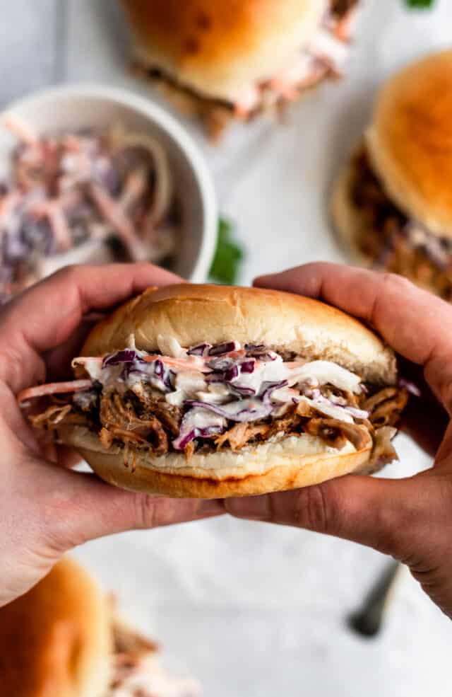 hands holding pulled pork sandwich with coleslaw