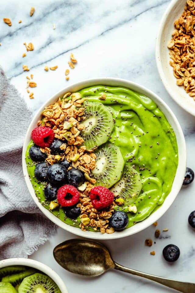 Green smoothie bowl topped with blueberries, raspberries, kiwi slices and granola.