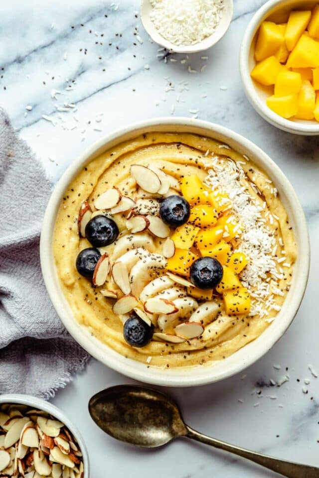 Smoothie bowl made with mango and topped with sliced almonds, blueberries and coconut.
