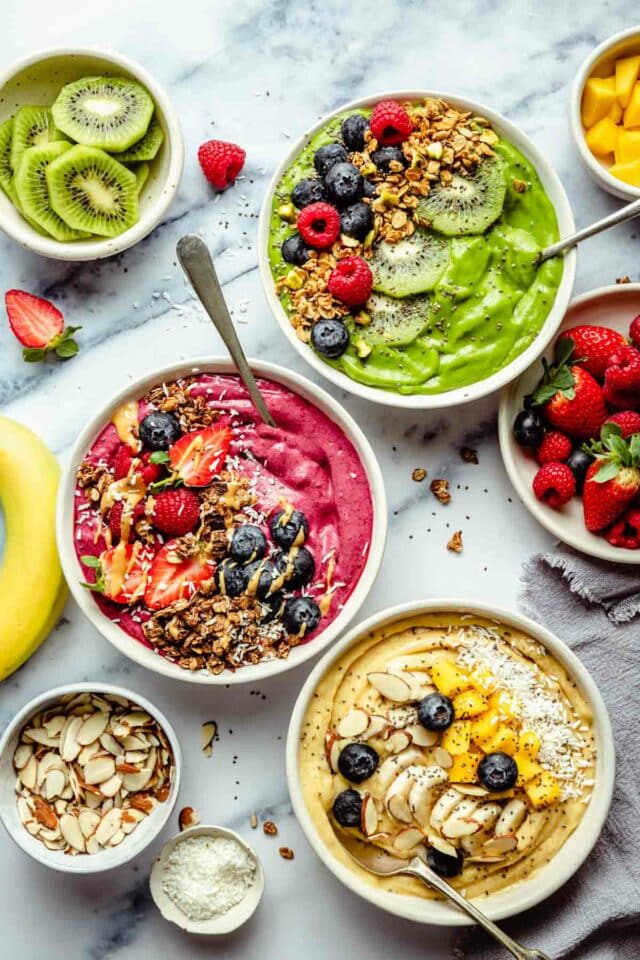 A green, berry and mango smoothie bowl topped with fruit and granola.