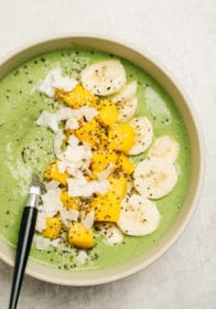 green smoothie bowl topped with fresh mango, coconut, sliced banana and chia seeds