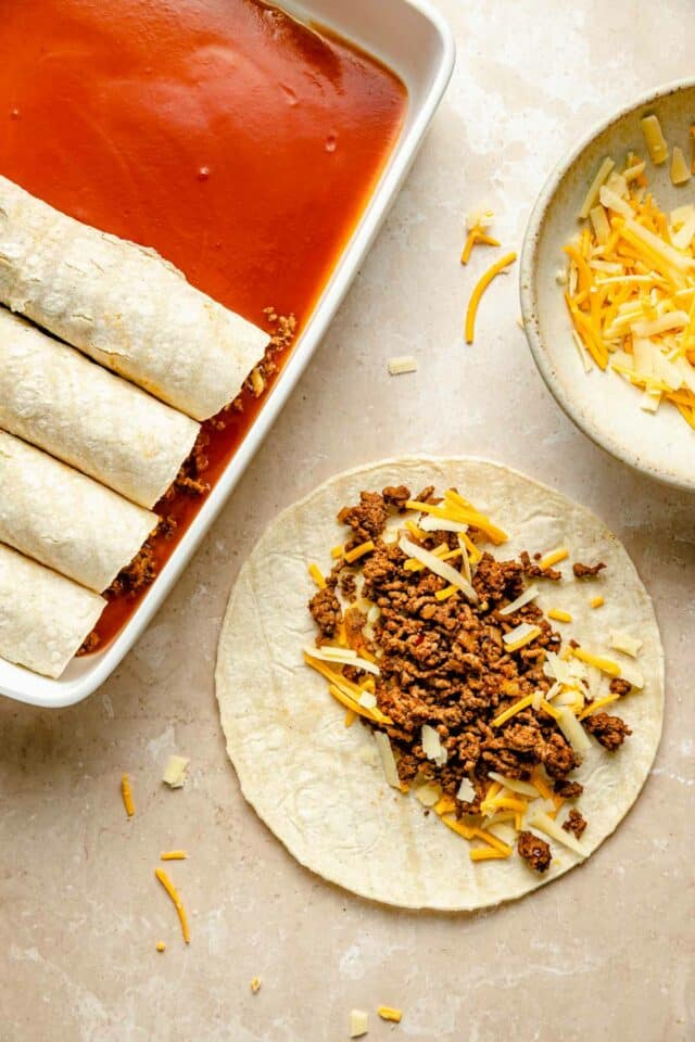 Adding ground beef and cheese to the center of tortillas and rolling them.