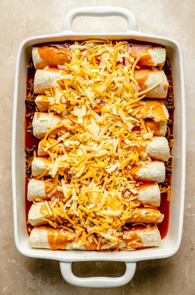 Tortillas rolled up in a dish and topped with enchilada sauce and shredded cheese.