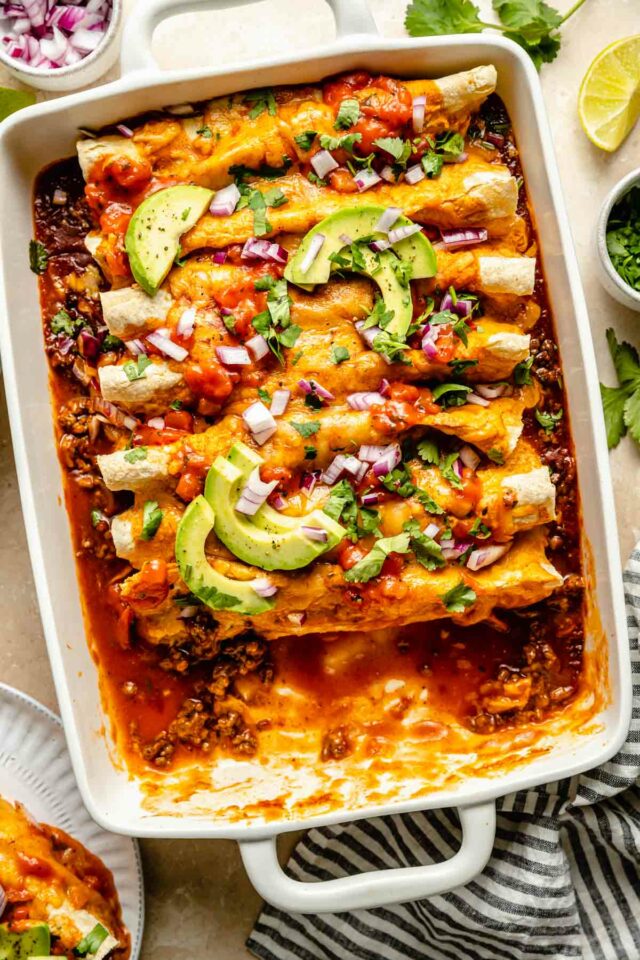 Cooked beef enchiladas in a white dish with a serving removed.