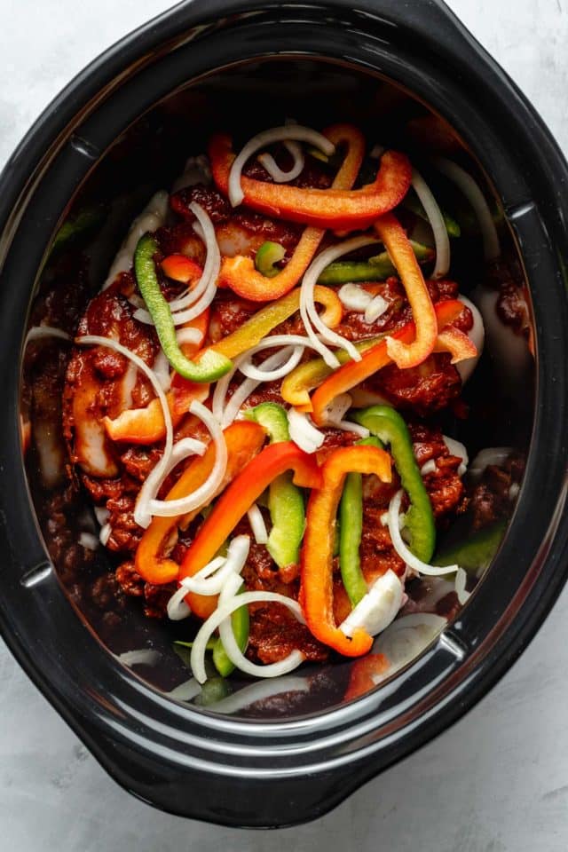 Adding sliced pepper and chicken to a slow cooker.