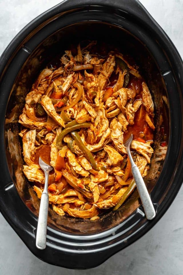 Cooked, shredded chicken with peppers in a slow cooker.