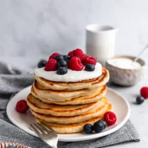 fluffy pancakes stacked on a white plate and topped with berries
