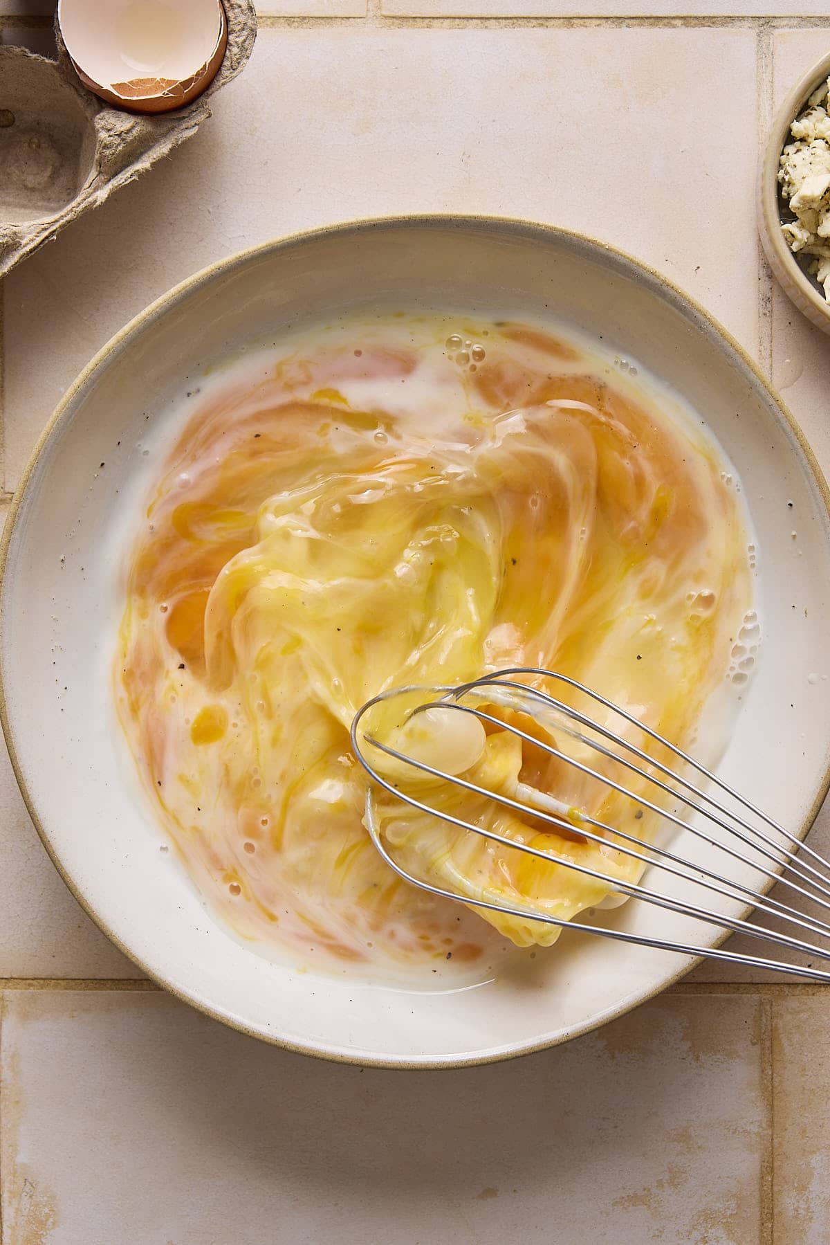 Whisking eggs with milk in a white bowl.