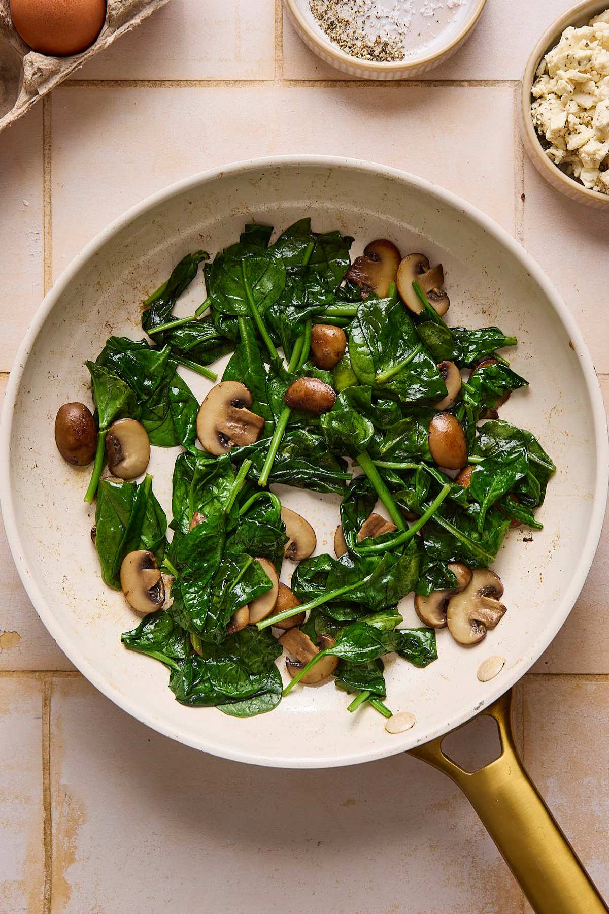 Spinach sautéing with mushrooms in a skillet.