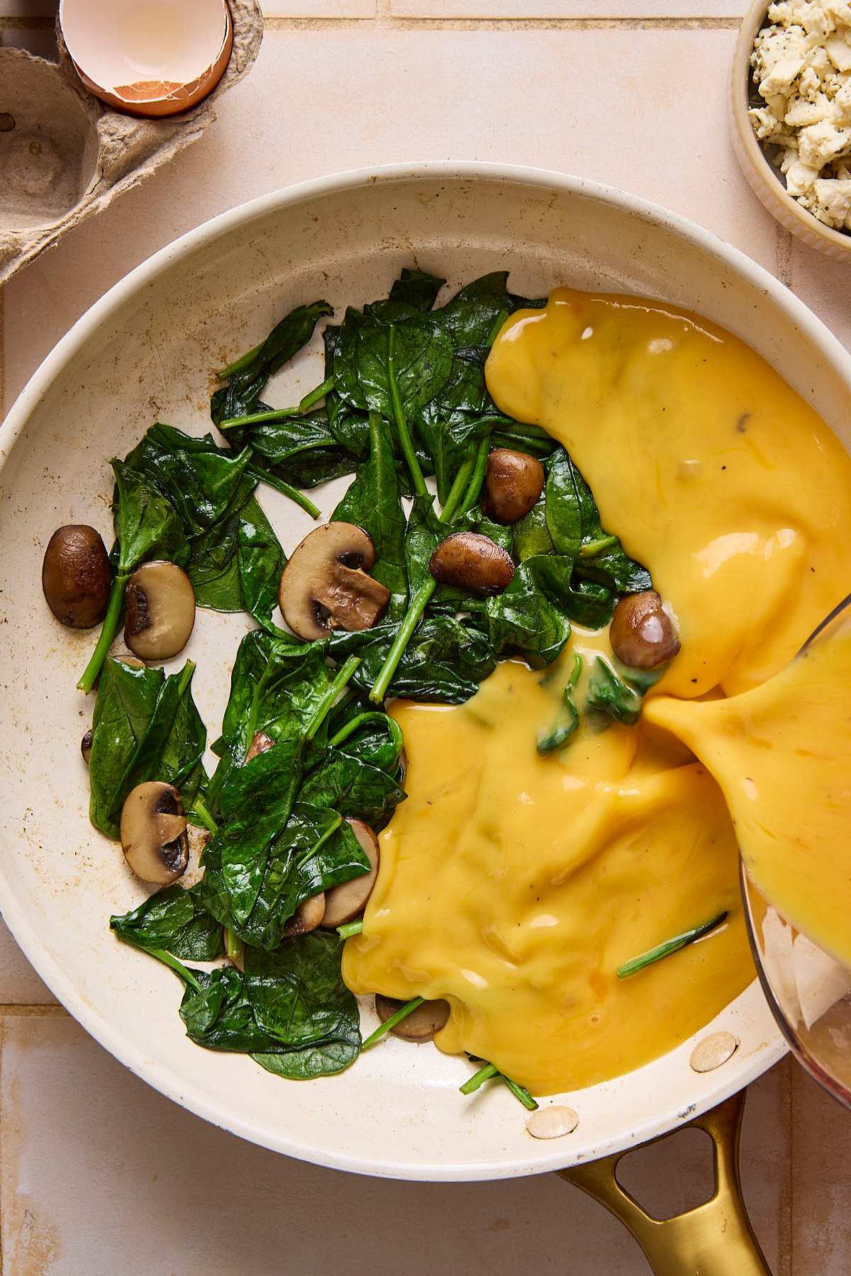 Pouring egg mixture into skillet with spinach and mushrooms.