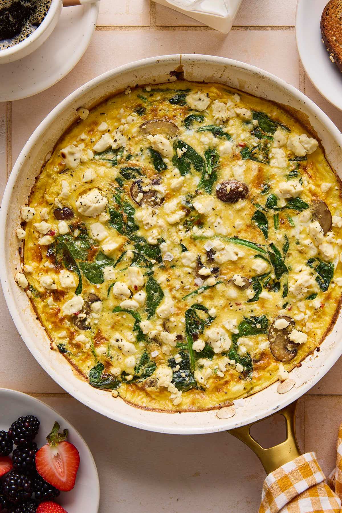 Cooked frittata recipe in a skillet near a cup of coffee and berries.