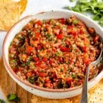 Homemade salsa served in a small white bowl with a spoon near chips.