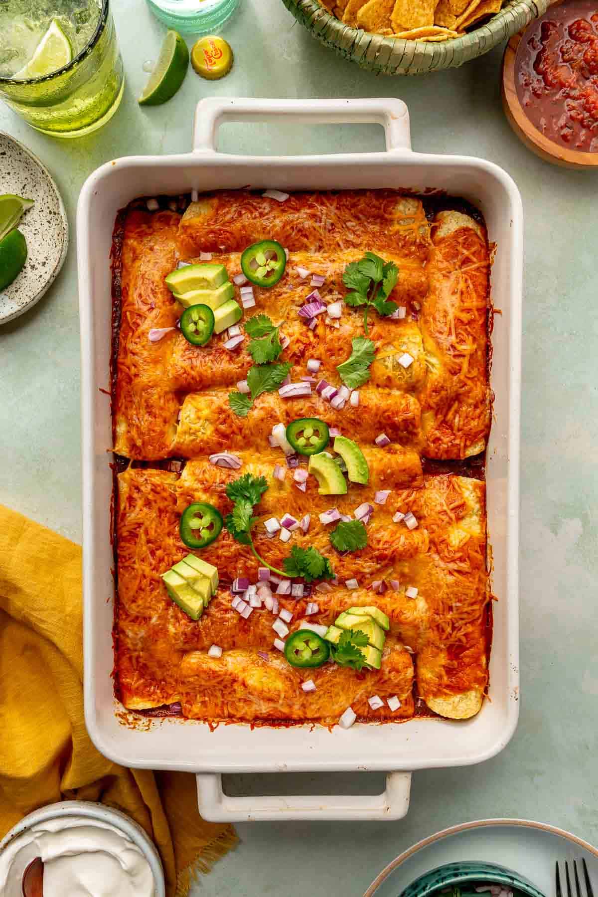 Veggie enchiladas in a white casserole dish topped with jalapeño slices and avocado.