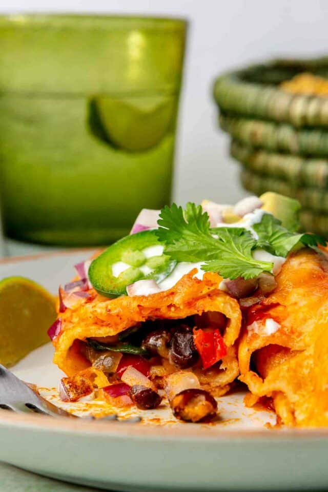 Veggie enchiladas on a plate topped with sour cream and jalapeños. 