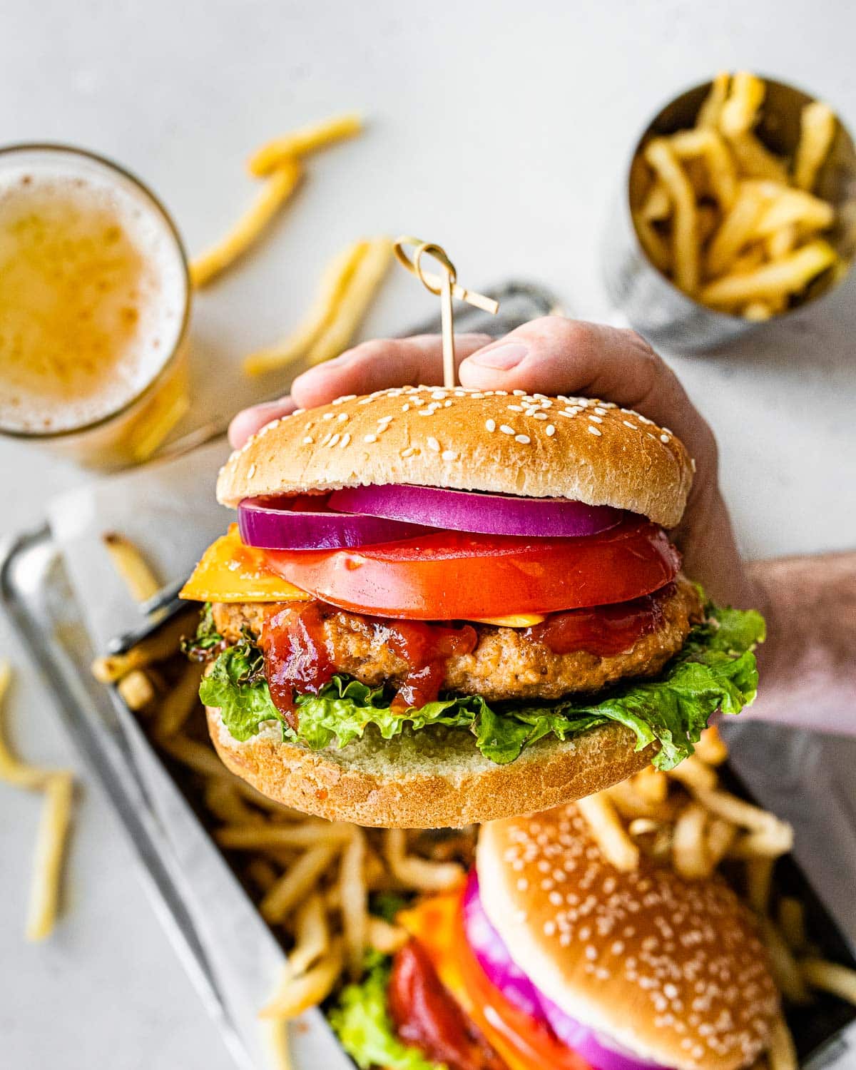Hand holding a burger with ketchup, lettuce, tomato and onion.