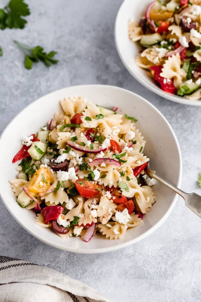 small white bowl filled with a pasta salad filled with tomato, cucumbers, red onion and feta